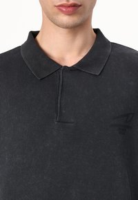 Dark charcoal polo shirt, made of soft fabric, with a ribbed collar, button placket, and a subtle logo on the left side. Smooth texture.