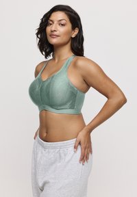 Sportieve groene sportbeha met gestructureerde stof met een geometrisch patroon, brede bandjes en een gladde band. Gecombineerd met grijze sweatpants.