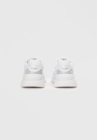 Hvite sneakers med en teksturert mesh-overdel og glatte sølvdetaljer på hælen. Har en polstret såle og snøring.