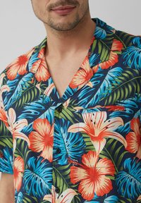 Camicia hawaiana con un vivace motivo floreale in rosso, arancione e blu su uno sfondo scuro. Maniche corte, chiusura con bottoni e dettaglio della tasca.
