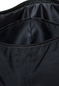 Interno di una borsa nera in nylon con texture liscia. Presenta una zip lungo il bordo superiore e cuciture strutturate per garantire durata.