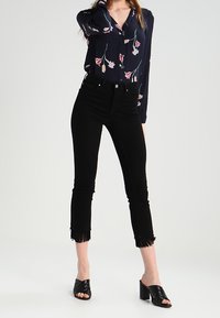 Blusa blu navy con motivo floreale, maniche lunghe e scollo a V; abbinata a jeans neri cropped con dettagli a frange all'orlo e mule open-toe.