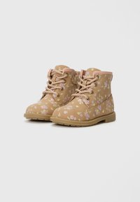 Bottes florales beige avec un design à lacets, accents beiges et tissu texturé présentant des motifs de fleurs roses et vertes. Semelles en caoutchouc plates.