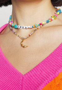 Kolorowe naszyjniki z koralikami o różnorodnych kształtach, w tym białe koraliki z literami układającymi się w słowo "SWEET", zawierające złoty wisiorek w kształcie półksiężyca.