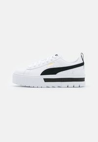 Baskets blanches avec une semelle plateforme épaisse, présentant des accents noirs, une bande noire texturée et un logo doré. Matériau lisse avec un design à lacets.