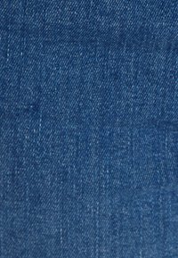 Tissu en denim de couleur bleue moyenne, présentant une texture lisse avec un motif de sergé subtil et un léger délavage dans certaines zones.