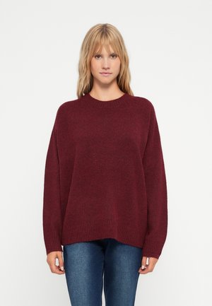Pull oversized bordeaux avec un col rond, bord-côte en bas et aux poignets, en matière tricot douce, associé à un jean bleu ajusté.
