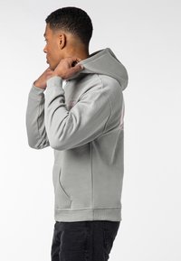 Gray hooded sweatshirt with ribbed cuffs and a front pocket. Features a small pink logo on the chest and a textured fabric finish.
