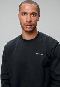 Sweatshirt noir en coton, avec un col rond, des poignets côtelés et un petit logo blanc Columbia sur la poitrine gauche.