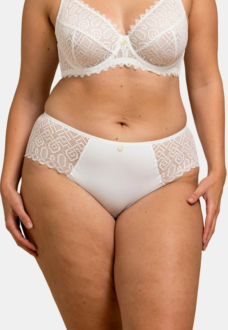 Ensemble de lingerie blanche comprenant un soutien-gorge en dentelle avec des motifs géométriques et une culotte assortie. La culotte possède des panneaux latéraux en dentelle et un bouton décoratif.