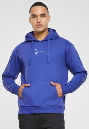 Blå hoodie i en ensfarvet farve med en frontlomme og et logo i hvidt. Blødt stof med ribbede mansjetter og nederste kant.