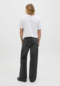 Pantaloni din denim negri cu picioare largi și buzunare spate, asociați cu un tricou simplu alb. Include un detaliu de curea cu ținte.