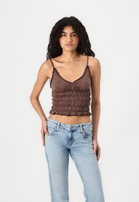 Top corto marrone con arricciature elastiche e bordi ondulati, abbinato a jeans dritti azzurri. Tessuto della superficie morbido.