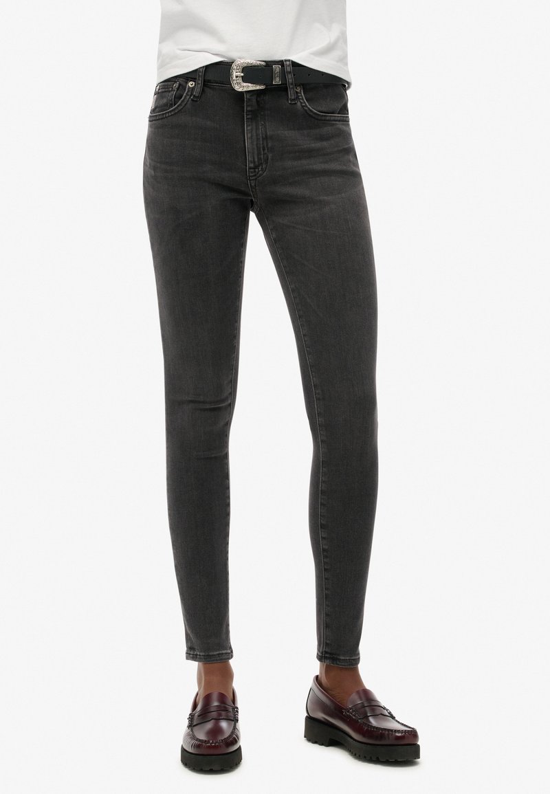 Jeans ajustados en denim gris oscuro, con un diseño clásico de cinco bolsillos y un cinturón con hebilla plateada. La tela tiene una textura sutil.