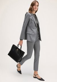 Szary dopasowany garnitur z elegancką marynarką i wąskimi spodniami. Czarna skórzana torebka na ramię z złotymi akcentami. Modelka nosi czarne, spiczaste baleriny.