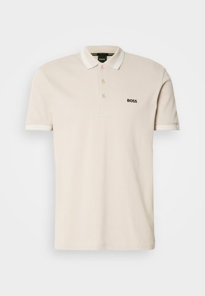 T-shirt polo beige avec un col, patte de boutonnage à trois boutons et logo noir brodé sur la poitrine gauche. Manches courtes avec accents blancs.