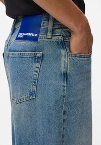 Light blue denim jeans with a straight-leg cut, featuring a blue label with "KARL LAGERFELD JEANS" and a small blue logo on the back pocket.