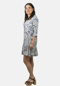 Vestido floral en tejido azul y blanco con falda acampanada, mangas tres cuartos y detalle de botones; combinado con tacones de plataforma negros con tiras.