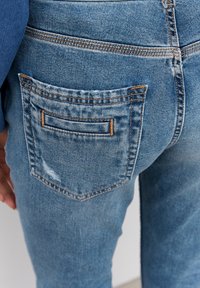 Jeans de mezclilla azul claro con un bolsillo trasero desgastado, presentando costuras en contraste y un diseño clásico de pierna recta.