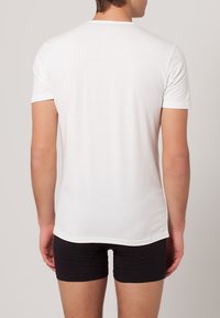 T-shirt bianco a maniche corte con un design semplice, texture liscia e collo rotondo, abbinato a pantaloni corti neri visibili in vita.