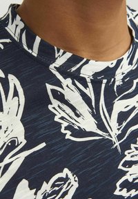 Tumedate t-särk, millel on valge lehekujundus, ümmargune kaelus ja pehme, tekstuuriga kangas. Suurendatud vaade kaelusele ja mustri detailidele.