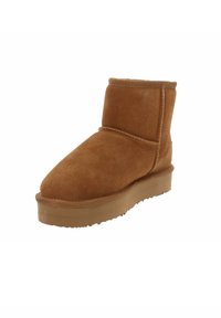 Stivaletto in suede marrone con punta arrotondata, dettagli cuciti e suola in gomma bassa. La texture sembra morbida e liscia.