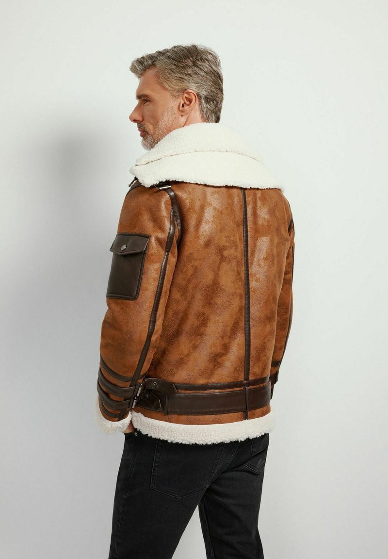 Giubbotto in pelle marrone con colletto in shearling e dettagli marroni. Presenta una tasca laterale e decorazioni a righe lungo le maniche.