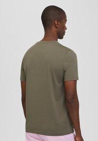 T-shirt corto verde oliva a maniche corte con scollatura rotonda e un piccolo dettaglio sul retro. Realizzato in un tessuto liscio con una forma aderente.