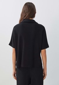 Zwarte korte mouwen overhemd met kraag, gemaakt van textuurstof, heeft een relaxte pasvorm en valt tot op taillehoogte, zichtbare naden op de schouders.