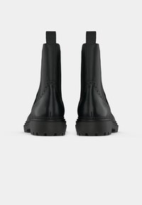 Mustad mustad kiilud sujuva nahkviimistlusega, külgmiste elastsete paneelidega ja robustsete, mustriliste kummitaldadega, mis sisaldavad kontrastseid õmbluse üksikasju.
