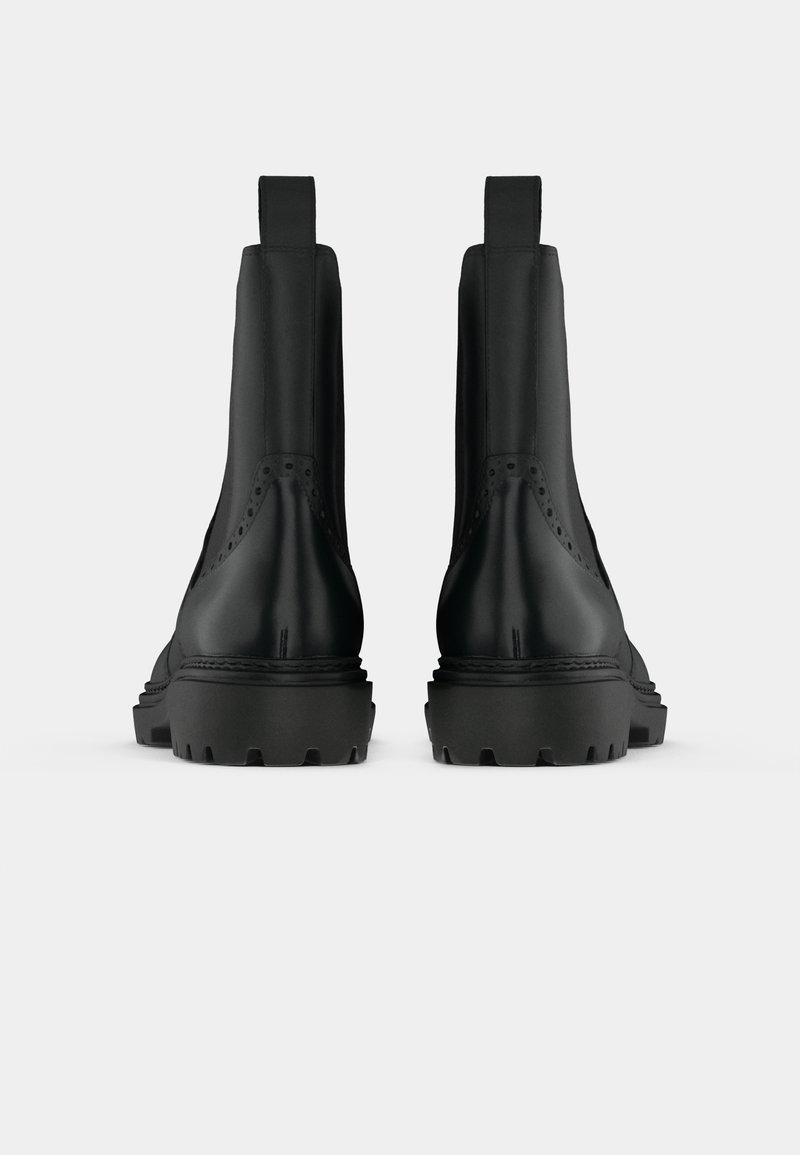 Schwarze Knöchelstiefel aus glattem Leder, mit seitlichen Elastikeinsätzen und robusten, gemusterten Gummisohlen, die kontrastierende Nähte aufweisen.