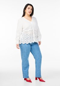 Vit blus med spetsdetaljer och knäppning, matchad med ljusblå strukturerade jeans och röda spetsiga klackar.