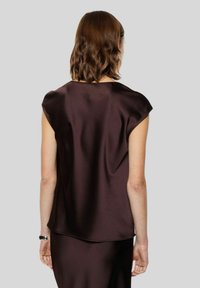 Top di satin marrone con maniche corte, texture liscia e scollatura tonda, visto dal retro. Sottile lucentezza e caduta.