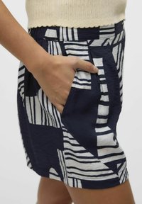 Jupe bleu marine avec des rayures abstraites blanches, dotée de deux poches latérales et d'une taille froncée. Tissu léger avec une finition texturée.