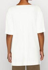 Camiseta blanca de gran tamaño hecha de tela suave. Corte relajado con mangas cortas y un escote amplio. Sencilla, sin estampados ni acentos.