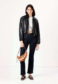 Giacca cropped in pelle sintetica nera, top aderente bianco, jeans a zampa scuri, borsa in stampa coccodrillo marrone e ballerine con stampa leopardata.