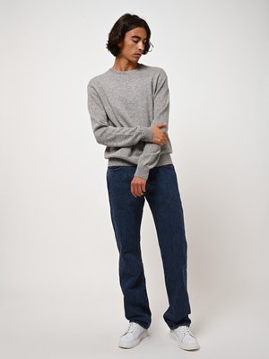 Lichtgrijze gebreide trui met een ronde hals, gecombineerd met donkerblauwe rechte jeans en witte sneakers. Eenvoudig en klassiek ontwerp.