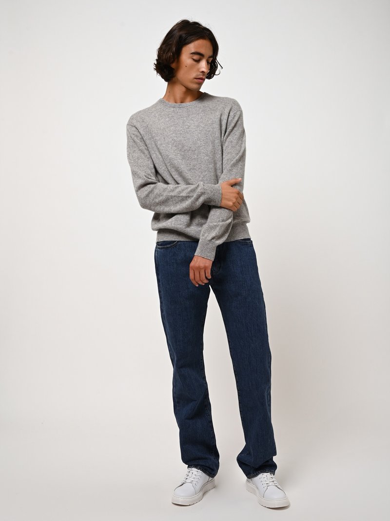 Maglione grigio chiaro a maglia con scollo rotondo, abbinato a jeans dritti blu scuro e sneaker bianche. Design semplice e classico.