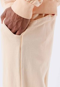 Pantalones de chándal color melocotón con una textura suave, que cuentan con un bolsillo lateral y puños acanalados. Diseño simple con líneas limpias.