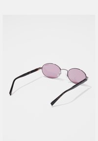 Occhiali da sole ovali con lenti rosa, montatura in metallo argento e steli in plastica nera a motivo. Design leggero, stile minimalista e morbidi cuscinetti per il naso.
