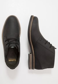Bottines en cuir noir à bout arrondi, surface texturée et lacets subtils. Présentent un talon empilé avec un accent en couches.