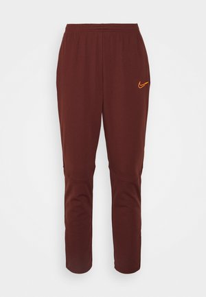 Braune Nike-Sweatpants mit elastischem Bund, enger zulaufenden Beinen und einem orangefarbenen Logodetail am linken Oberschenkel. Weicher Stoff.
