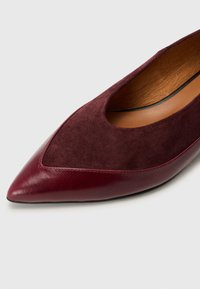 Ballerine bordeaux à bout pointu avec un mélange de cuir lisse et de daim. Présente un design découpé près de l'arche et une doublure intérieure douce.