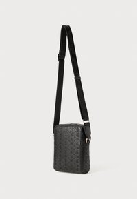Svart crossover bag med preget logo-design, rektangulær form, glidelås-lukking og justerbar stropp med logodetaljer.