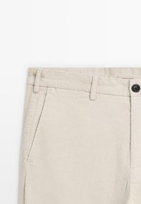Light beige corduroy pants featuring a flat front, belt loops, a zip fly with button closure, and two side pockets.