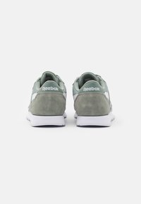 Un par de zapatillas Reebok grises y blancas vistas desde atrás sobre un fondo blanco liso.