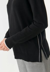 Schwarzer Pullover mit langen Ärmeln, mit weißen Akzenten an den Bündchen und Seitennähten. Hergestellt aus einem weichen Material, hat eine lockere Passform und einen gerippten Saum.