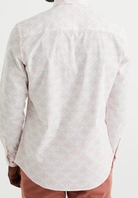 Camisa blanca de manga larga con un delicado patrón en rosa pastel que presenta formas abstractas. Tejido suave con cuello estándar y puños abotonados.
