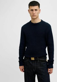 Navy knit sweater with a textured pattern, round neckline, and long sleeves, paired with dark jeans and a black belt with a gold accent.