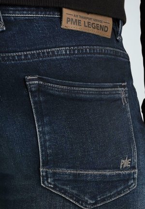 Dark denim jeans featuring a back pocket with white stitching, a brown leather label marked "PME LEGEND," and a distressed texture.